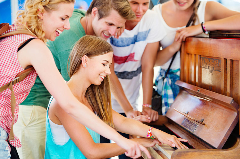 Teens gathered around a piano enjoying music